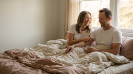 Stel drinkt lachend koffie op bed terwijl de partner een hand op zijn arm legt