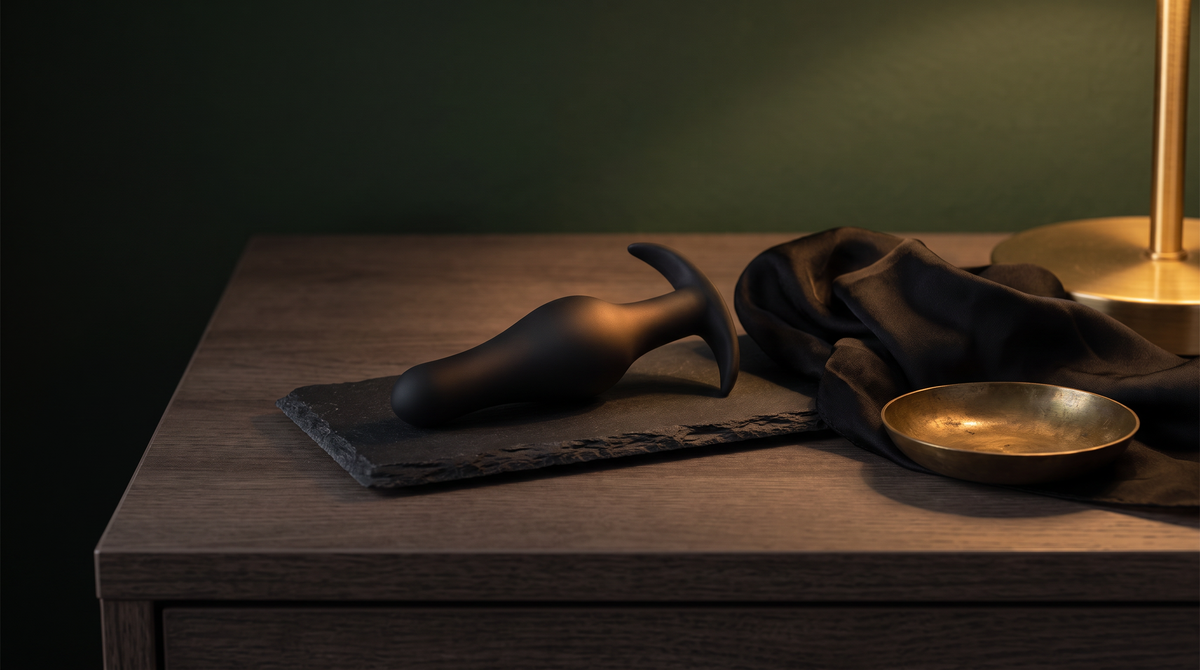 Zwarte siliconen buttplug met handgreep op een leistenen plateau naast een zijden sjaal