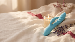 Lichtblauwe rabbit vibrator van zacht siliconen op een linnen laken naast een kaars