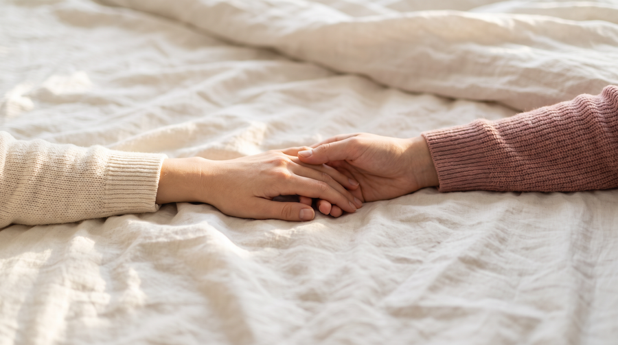Twee handen die elkaar losjes vasthouden op zachte linnen lakens in ochtendlicht: vaginisme samen aanpakken