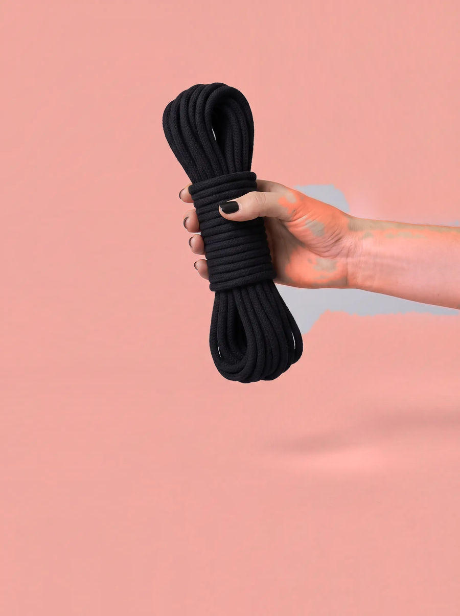 Een hand houdt een opgerold zwart katoenen touw tegen een terracottarode achtergrond