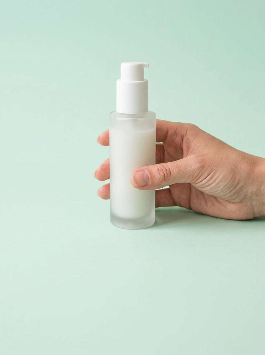 Een hand houdt een blanco pompflacon tegen een mintgroene achtergrond
