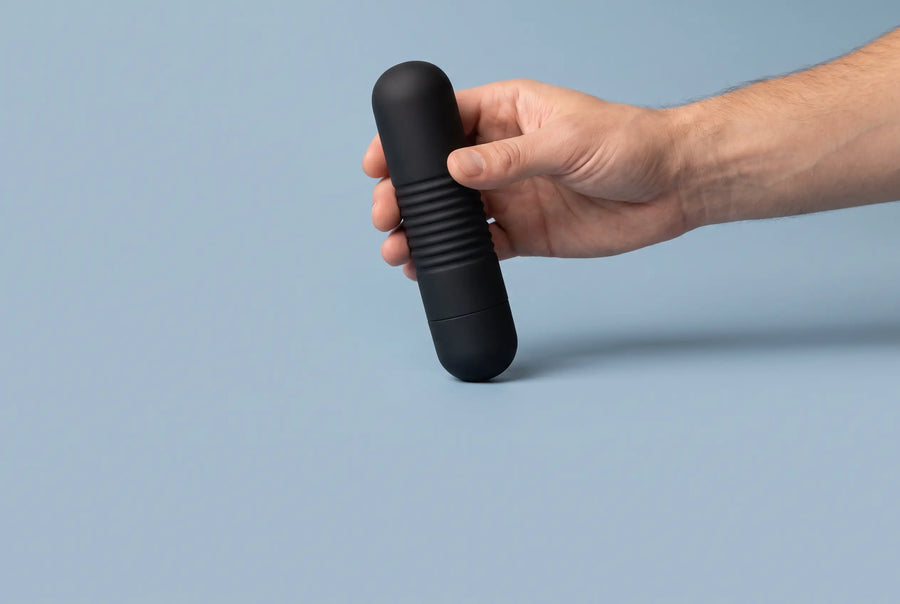 Een hand houdt een mat zwarte massager tegen een staalblauwe achtergrond