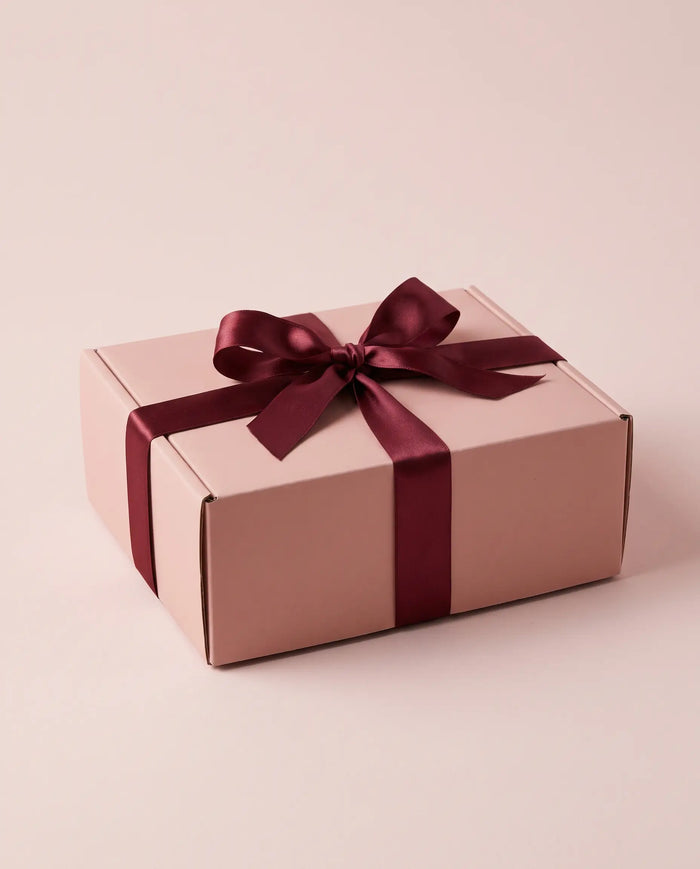 Een gesloten roze cadeaudoos met een wijnrood satijnen lint