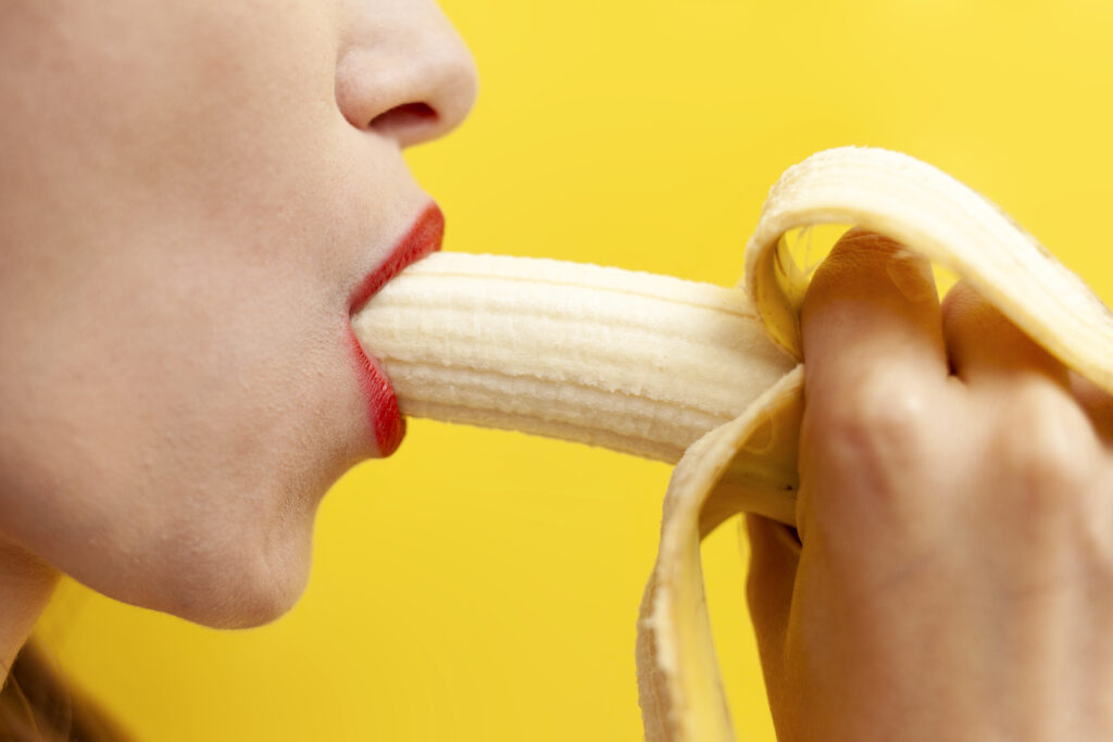 sexy intimate blowjob concept woman licks takes banana her mouth yellow background kopie